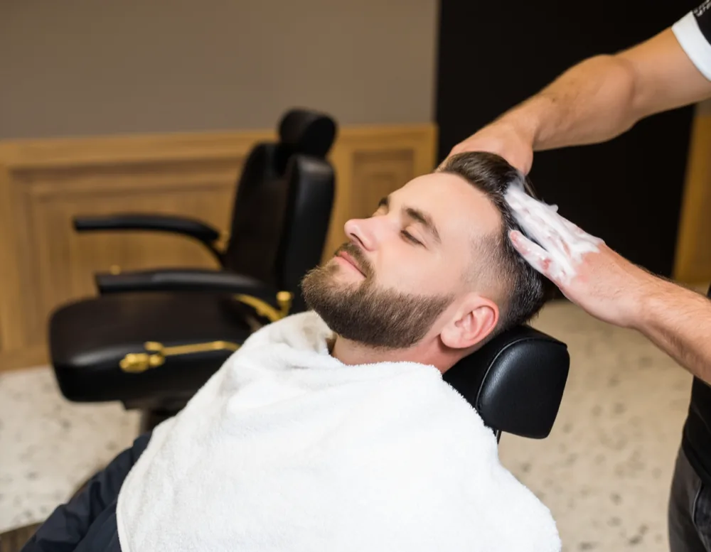 A hot towel being laid over a reclined client’s scalp before a head shave